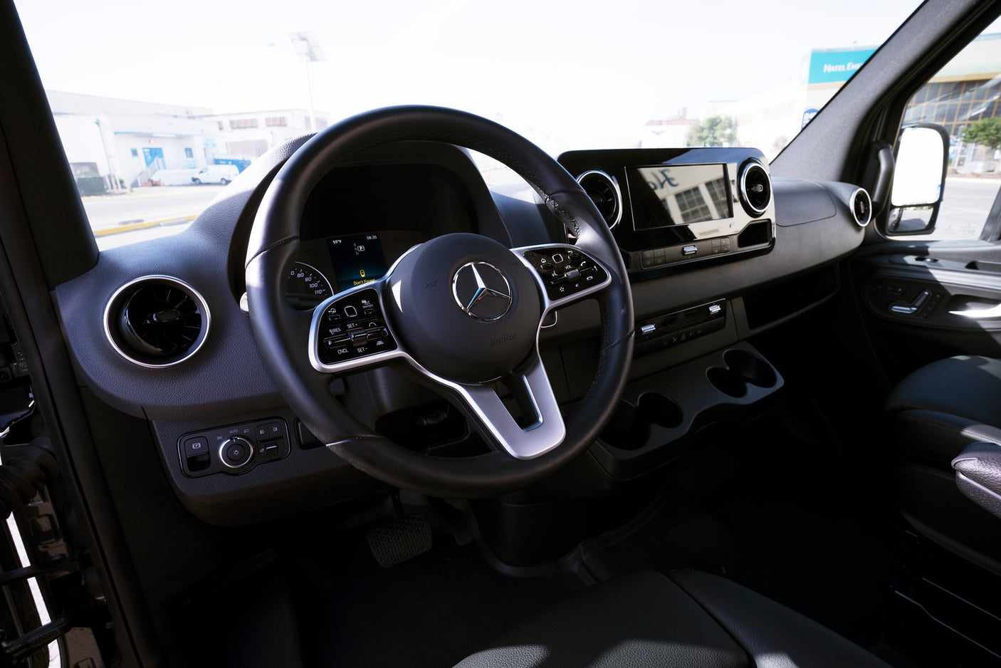 Driver's seat view of a modern Mercedes-Benz Sprinter van interior, with dashboard, steering wheel, and screens. Ideal for an rv rental.