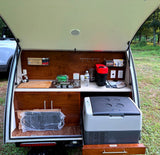 Compact RV rental teardrop trailer outdoor kitchen with Nespresso, stove, and cooler, perfect for camping.