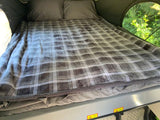 Cozy RV rental bed with a soft plaid blanket and pillows. Enjoy nature from your comfortable camper.