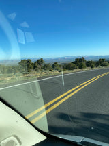 Road trip view from an RV rental: open highway, a distant mountain range, and trees under a clear blue sky.