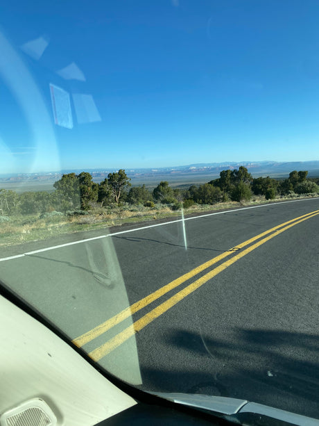 Road trip view from an RV rental: open highway, a distant mountain range, and trees under a clear blue sky.