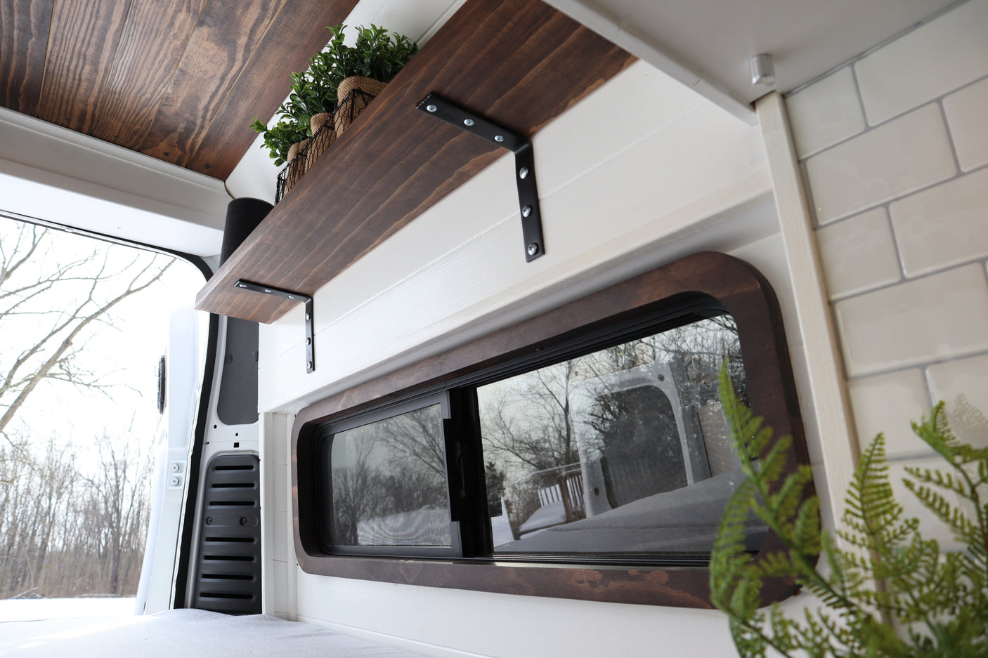 Cozy wood and white camper van rental interior with a custom shelf and snowy window view.