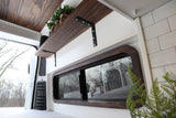 Cozy wood and white camper van rental interior with a custom shelf and snowy window view.