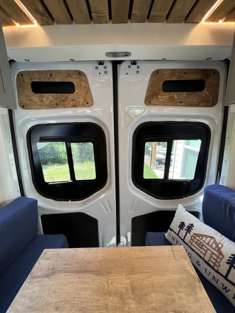 Relaxing RV rental interior with cozy dinette, wood ceiling & rear windows opening to nature. Perfect camper van view.