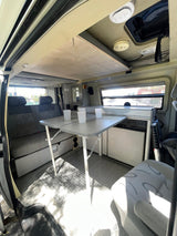 This RV rental interior features a versatile dining table, bench seating, and compact mini-fridge. Practical compact camper setup.