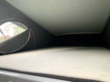 View inside an RV rental's pop-up roof tent, showing a comfortable white mattress and a window with trees outside.