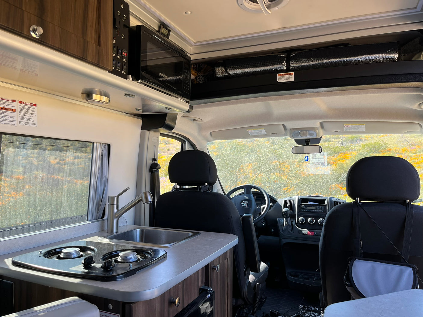 RV rental interior shows a compact kitchen with stovetop, sink, microwave, and the front cab area.