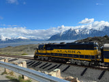 Scenic Alaska: A blue and yellow train, number 3009, with snow-capped mountains and water. An RV rental is perfect for exploring here.