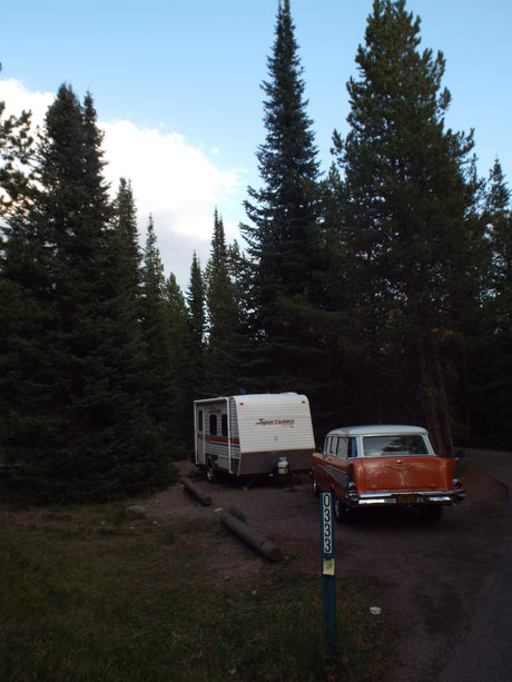 Campsite scene featuring an RV rental, a classic car, and tall evergreen trees. Perfect for camping!