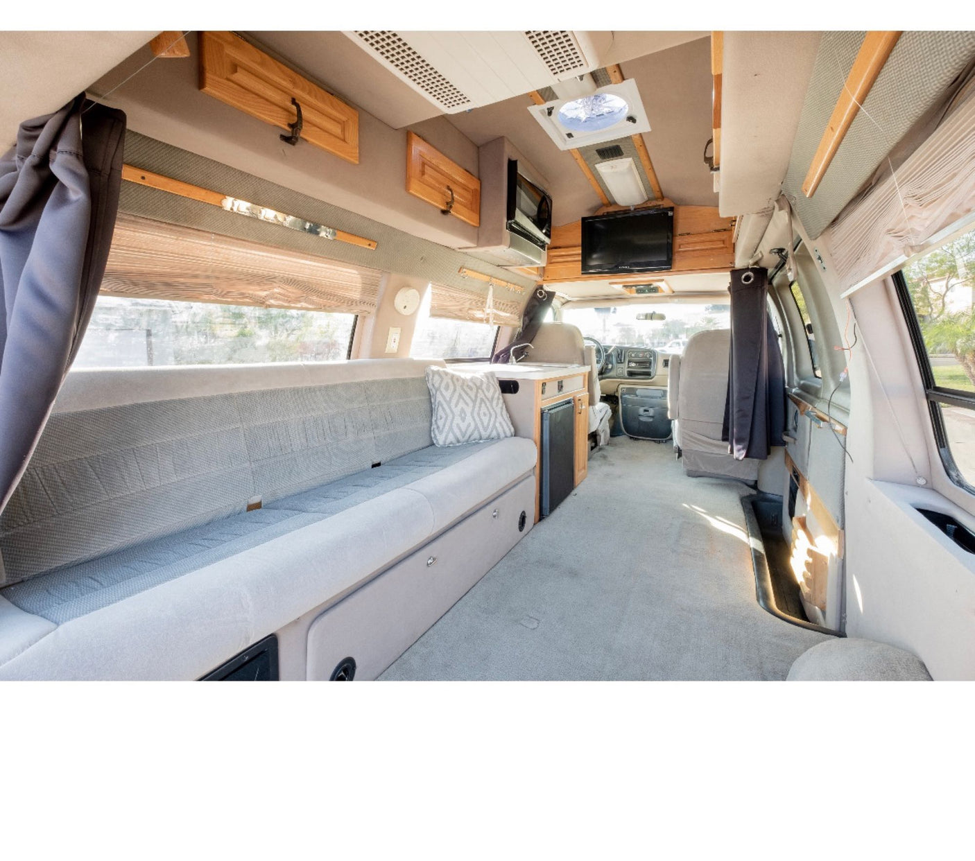 Inside this rv rental: cozy living space with grey seating, kitchenette, TV, and wood cabinets.