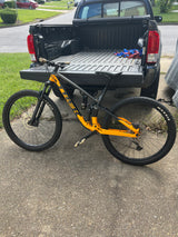 An orange/black mountain bike rests next to a pickup truck. Ideal transport for outdoor adventures, perfect alongside an RV rental trip.