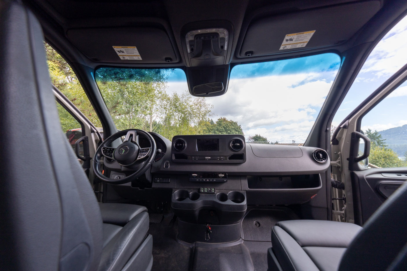 Inside an RV rental, the van's modern dashboard, steering wheel, and front seats with a clear view ahead.