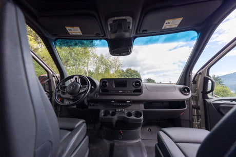 Inside an RV rental, the van's modern dashboard, steering wheel, and front seats with a clear view ahead.