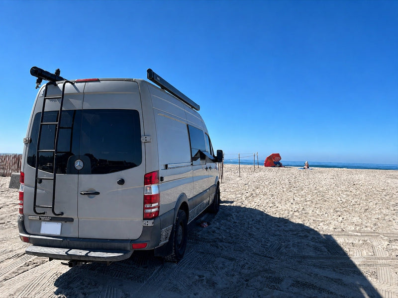 RV rental camper van parked on a sunny sandy beach. Ocean and people relaxing under an orange umbrella in the distance.|Spacious RV rental interior featuring a kitchenette — photo 1