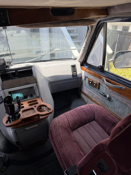RV rental front cabin showing a custom wooden console, grey dashboard, and maroon passenger seat, with a view through the windshield.