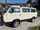 Classic white VW camper van, ideal for your next RV rental. Parked on a paved driveway under a blue sky.