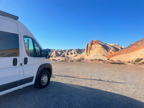 RV rental parked in a stunning desert landscape with vibrant, layered rock formations under a clear sky. Perfect for a road trip!