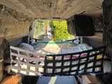 RV rental interior: Cozy camper bed with safety net, colorful blanket, wood paneling, and a green outdoor view.