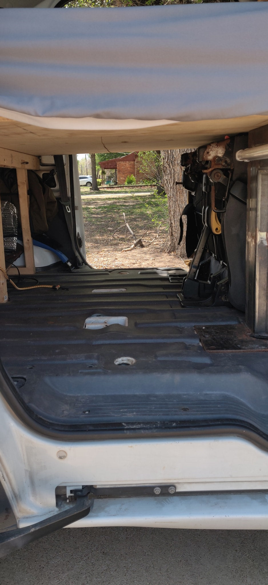 View from inside an RV rental looking out the back. The van's interior shows a basic floor, wooden frame, and exposed seat mechanism. — photo 8