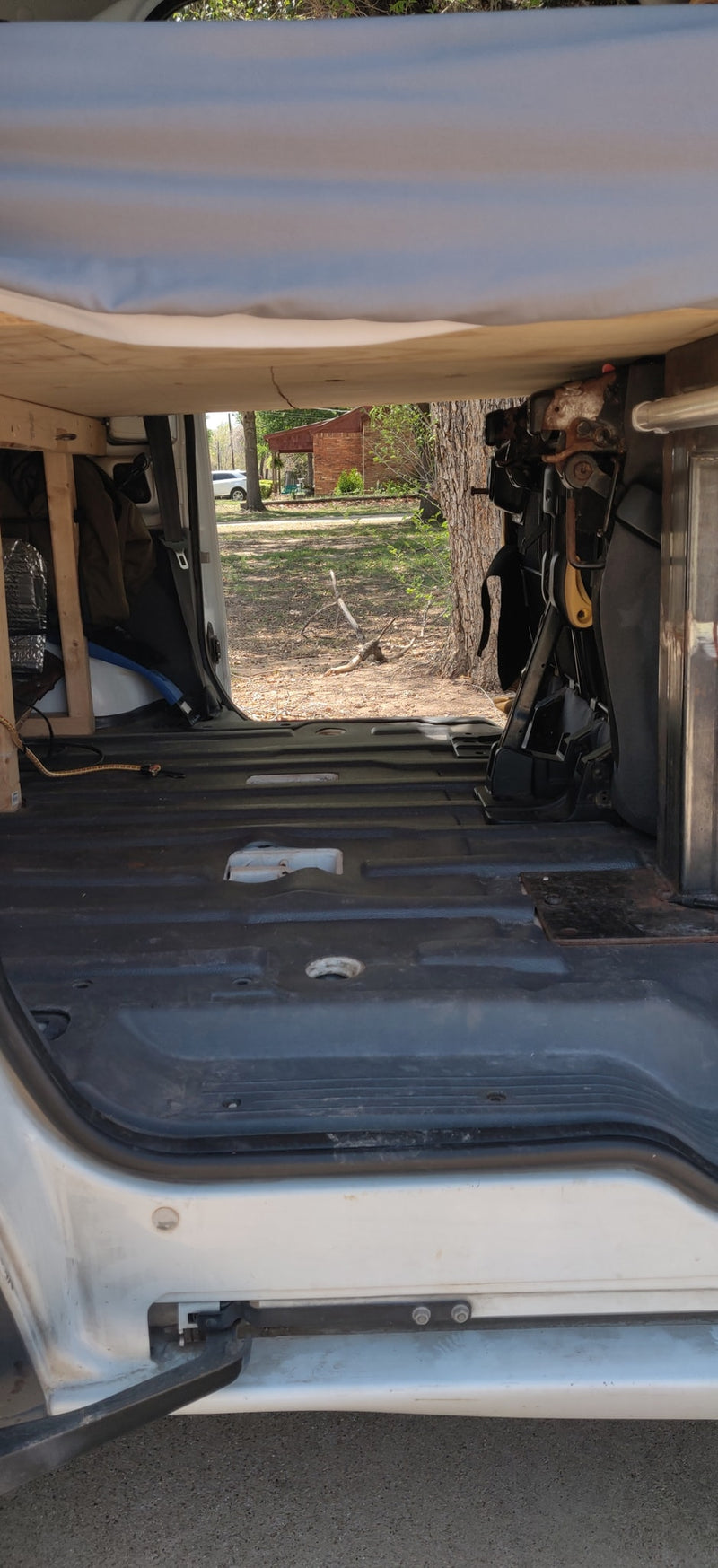 View from inside an RV rental looking out the back. The van's interior shows a basic floor, wooden frame, and exposed seat mechanism. — photo 8