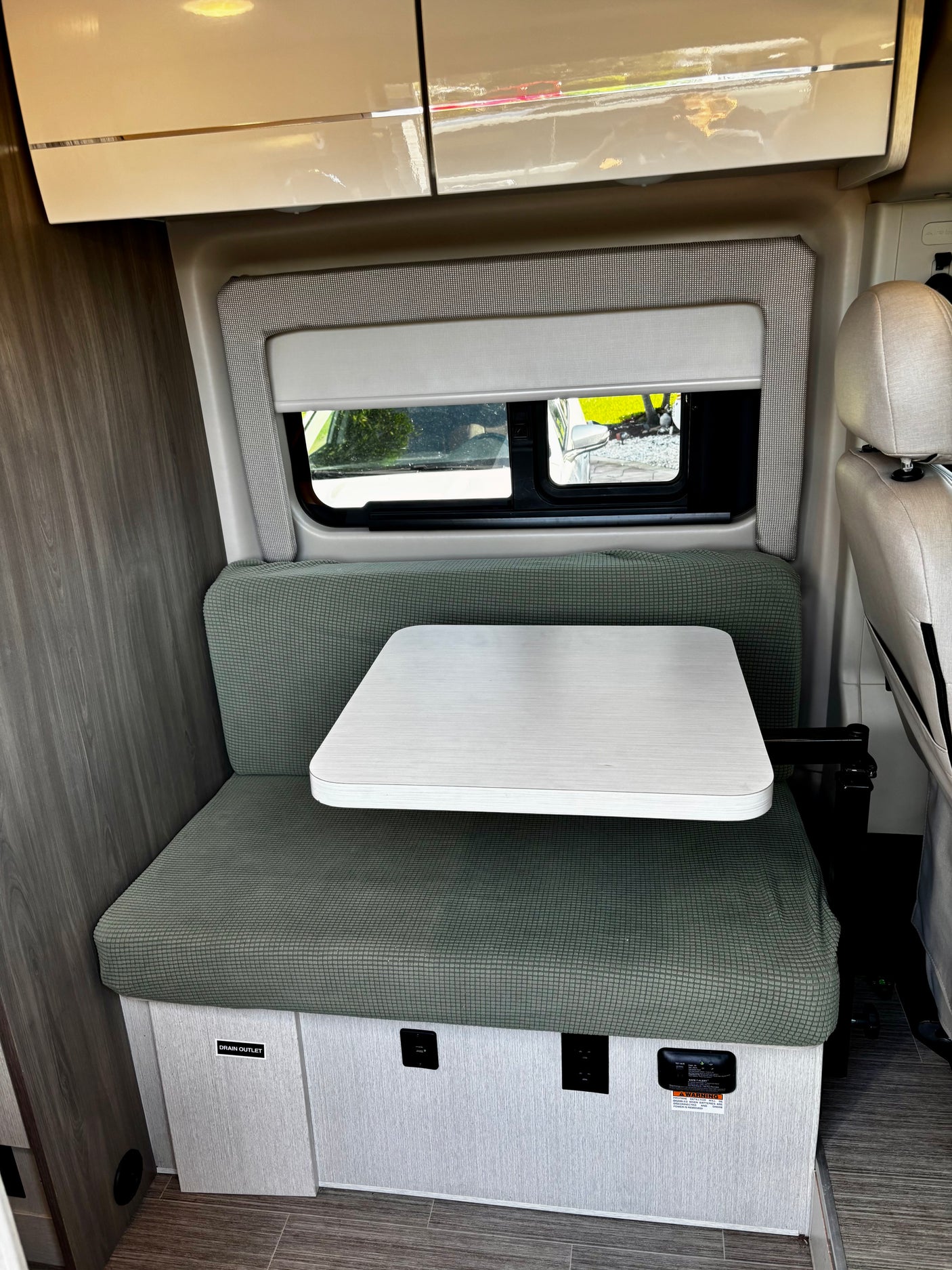 Inside an RV rental: a cozy dinette with green seating, adjustable table, window, and accessible power outlets.