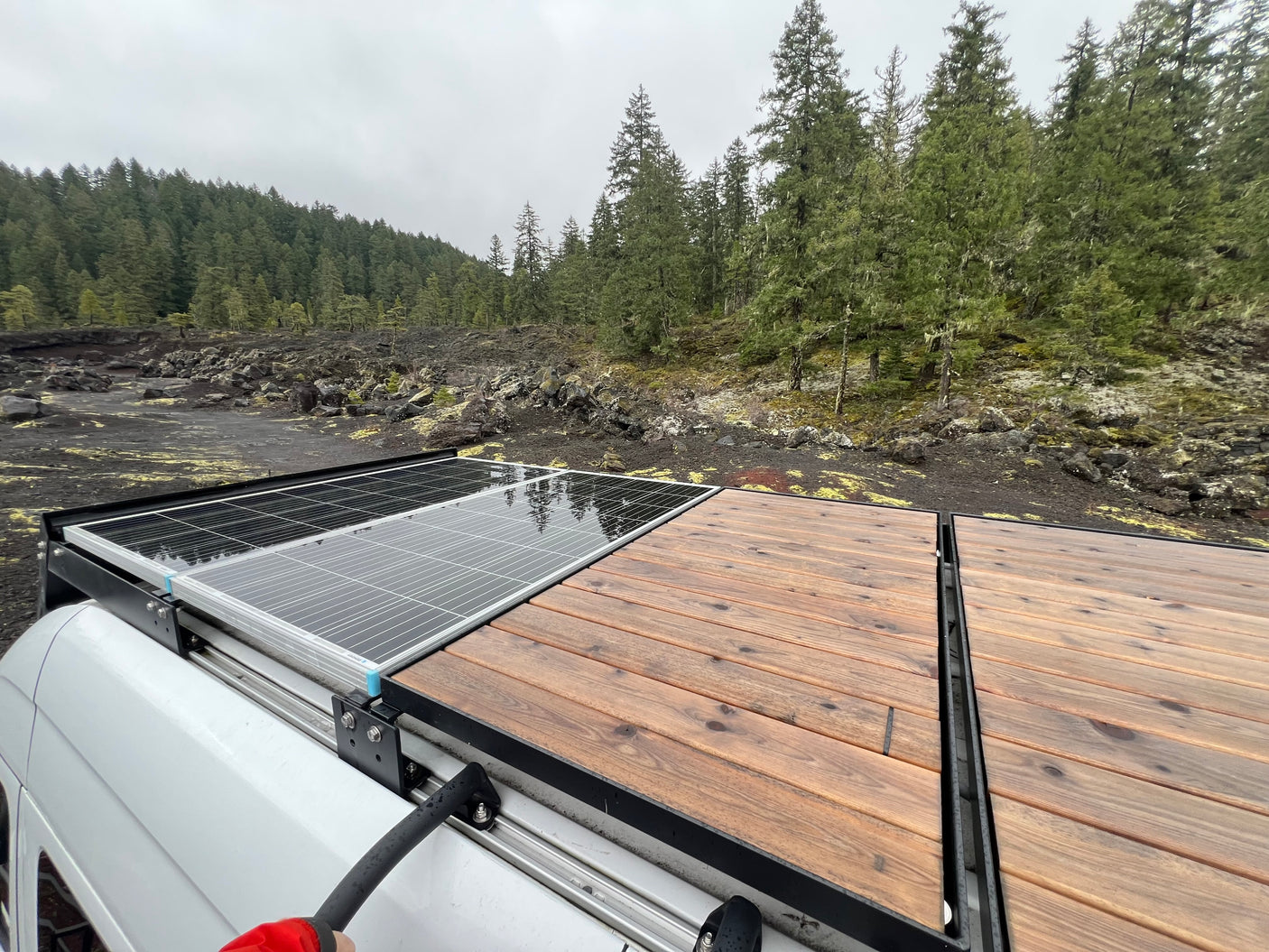 RV rental with solar panels & wood roof deck, overlooking a lava field and forest on a cloudy day.