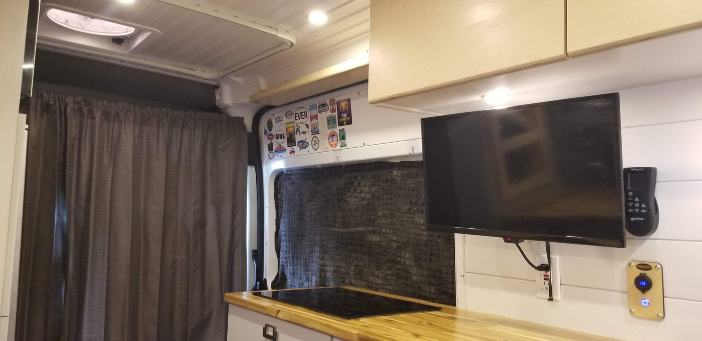 Inside a cozy RV rental: sleek kitchenette with induction cooktop, wall-mounted TV, and bright interior lighting.