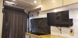 Inside a cozy RV rental: sleek kitchenette with induction cooktop, wall-mounted TV, and bright interior lighting.
