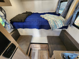 Cozy RV rental interior: elevated bed, dinette seating, and compact kitchen area for travel comfort.