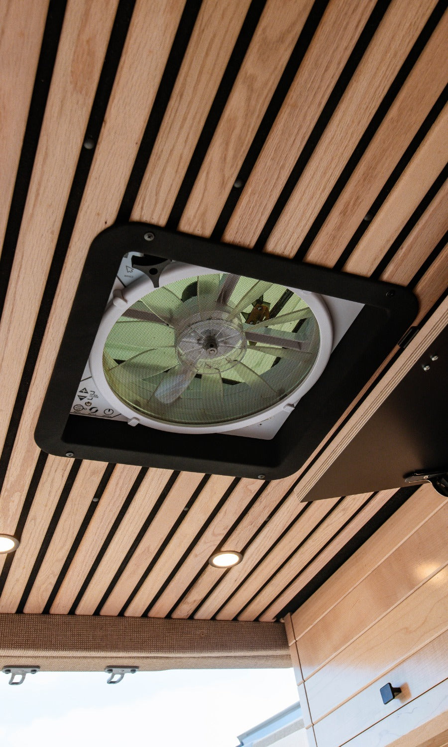 Modern RV rental interior showing a wooden slatted ceiling with a large ceiling vent fan, recessed LED lights, and a cozy, functional design.