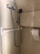 RV rental compact bathroom with a handheld shower, water controls, a white support bar, and a toilet paper holder.