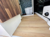 RV rental: Modern light wood flooring connects a wood countertop to a compact toilet with blue hexagonal tiles.