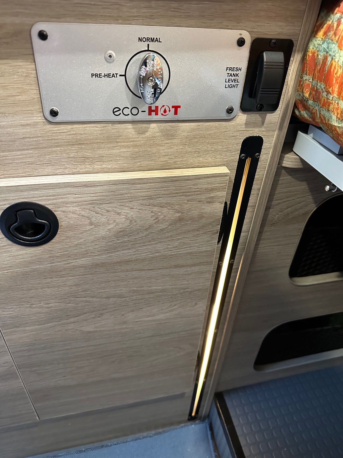 RV rental interior shows Eco-HOT water heater controls & fresh tank light, with wood panels, cabinet latch, and LED lighting.