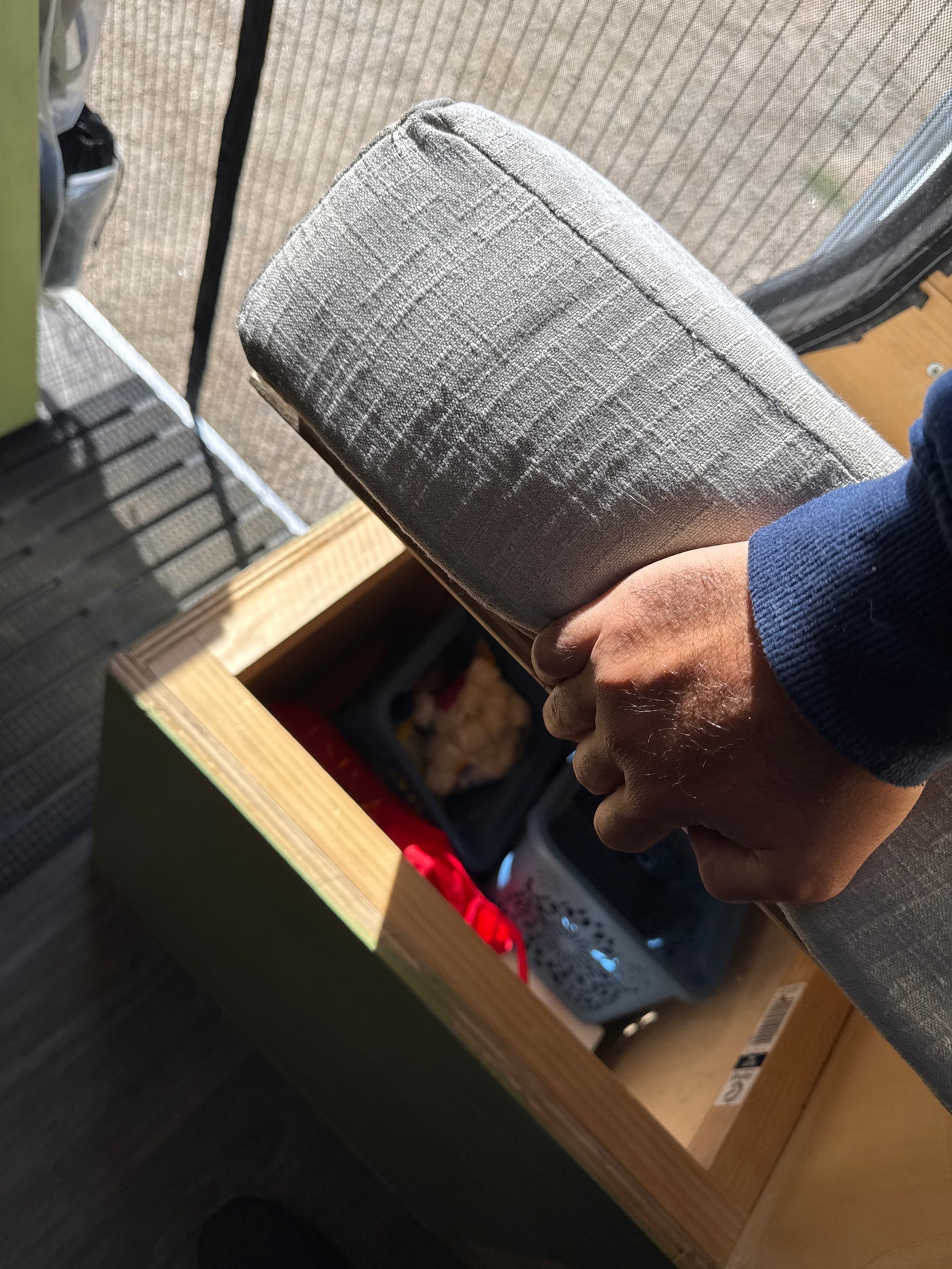 Person's hand places a grey cushion onto a wooden storage unit, revealing organized bins below, ideal for RV rental use.