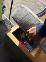 Person's hand places a grey cushion onto a wooden storage unit, revealing organized bins below, ideal for RV rental use.