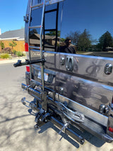 Dark grey RV rental with rear ladder and bike rack, perfect for outdoor adventures. A person is reflected in the window.