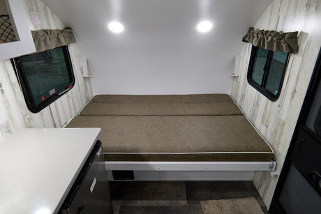 RV rental interior: cozy bed, side windows, and compact counter with fridge. Perfect for your next adventure.