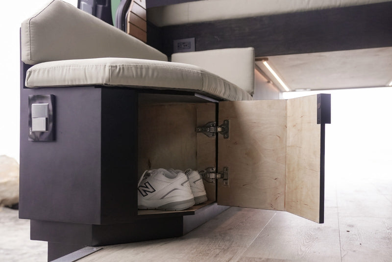 This RV rental features smart interior storage. A dark bench unit has an open door revealing white shoes inside, with switches on the side. — photo 8