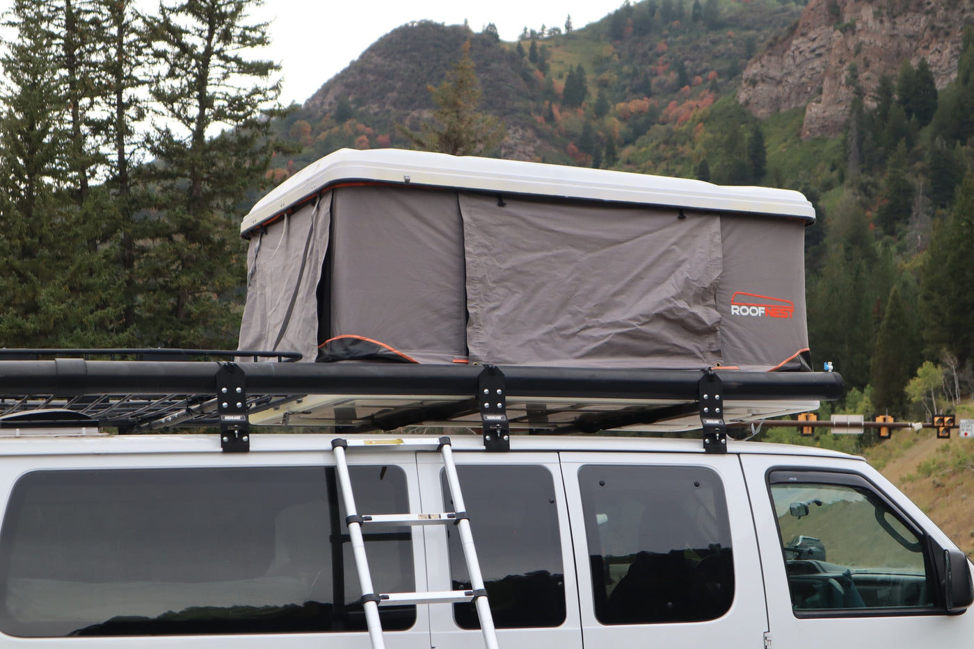 RV rental van with an open Roofnest rooftop tent and ladder, parked against a backdrop of mountains and fall trees. — photo 7