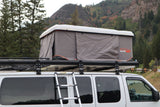 RV rental van with an open Roofnest rooftop tent and ladder, parked against a backdrop of mountains and fall trees.