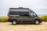 This gray RIZE Ram ProMaster RV rental is parked on a dirt road with yellow flowers and the ocean in background.