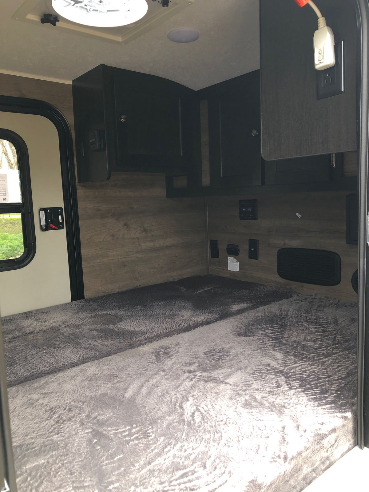 Cozy RV rental interior with a comfy gray bed, overhead cabinets, power outlets, and a window for a comfortable stay. — photo 4