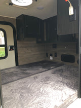 Cozy RV rental interior with a comfy gray bed, overhead cabinets, power outlets, and a window for a comfortable stay.