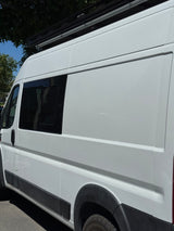 Side view of a white camper van RV rental with a tinted window and roof rack system.