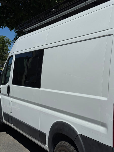 Side view of a white camper van RV rental with a tinted window and roof rack system.