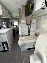 Bright RV rental interior features a functional kitchenette, comfortable seating with seatbelts, and a wall-mounted TV for your journeys.
