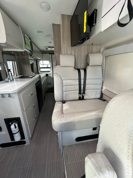 Bright RV rental interior features a functional kitchenette, comfortable seating with seatbelts, and a wall-mounted TV for your journeys.