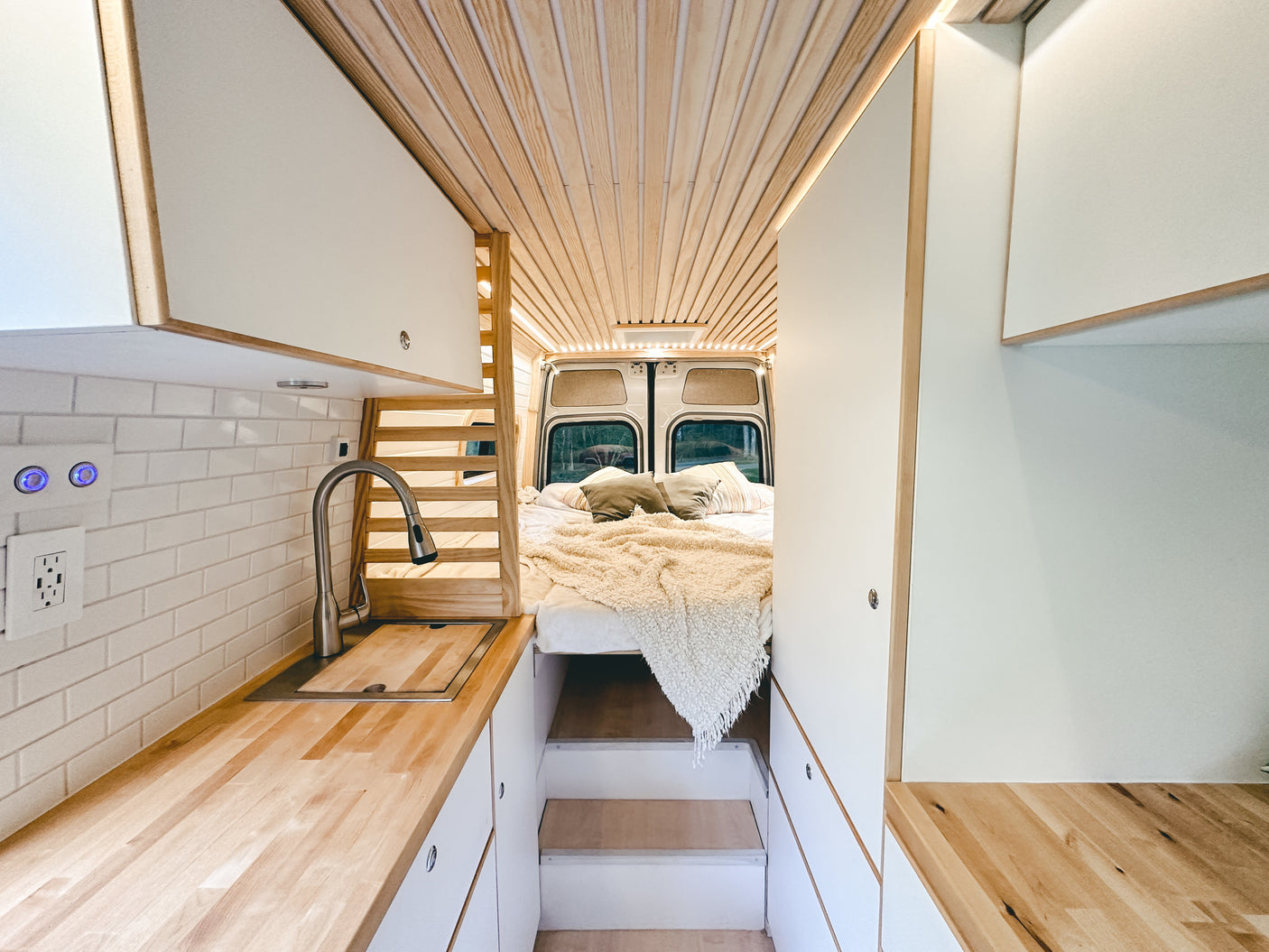 Explore this stylish RV rental's interior: a kitchen with wood counters, subway tile, and a cozy bed with wood-slat ceiling.