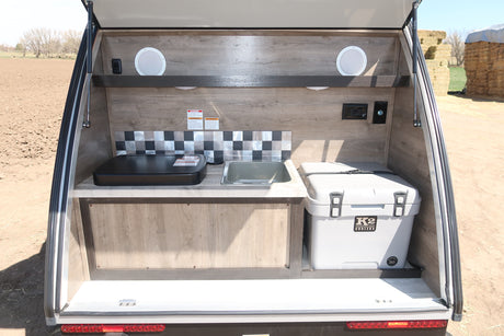This RV rental's outdoor kitchen features a griddle, sink, and K2 cooler, perfect for camping and outdoor adventures.