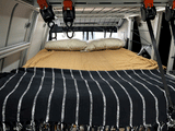 Inside an RV rental: A tidy bed with pillows and a striped blanket, plus handy overhead storage.